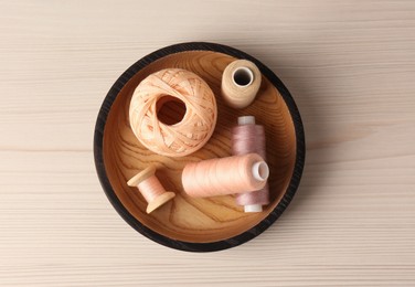 Photo of Bowl with color sewing threads on wooden table, top view