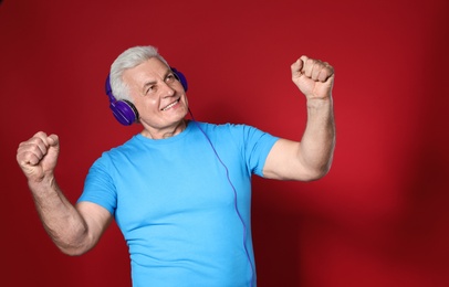 Photo of Mature man enjoying music in headphones on color background