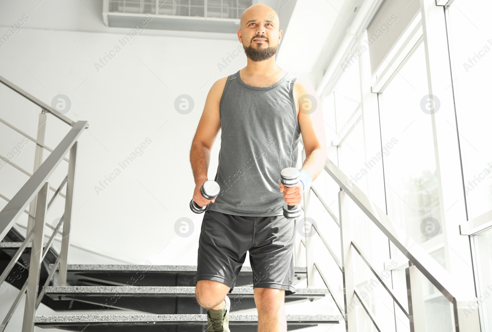 Photo of Overweight man running with dumbbells on stairs indoors