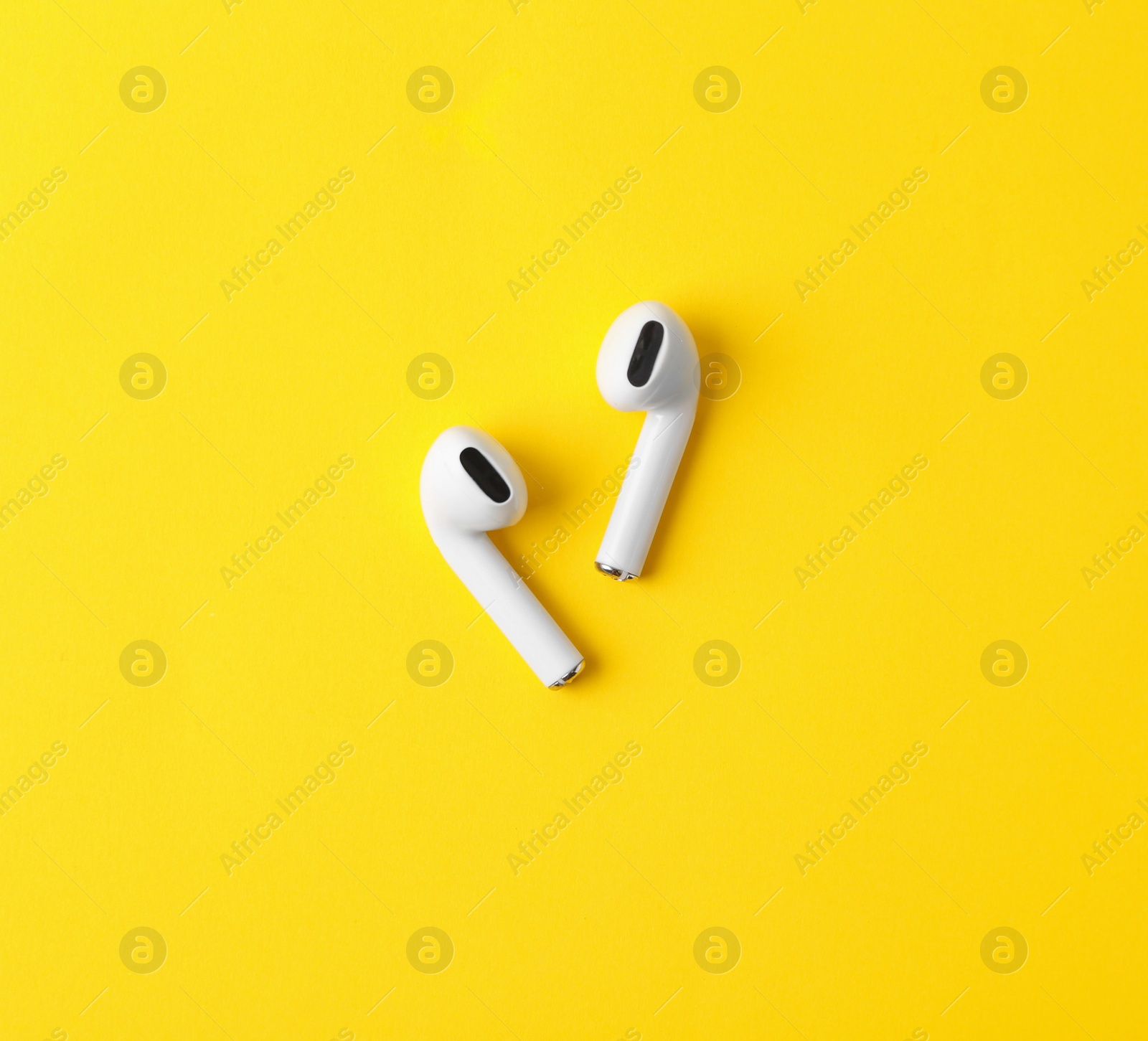 Photo of Modern wireless earphones on yellow background, flat lay