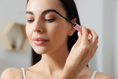 Photo of Beautiful young woman applying mascara indoors, closeup