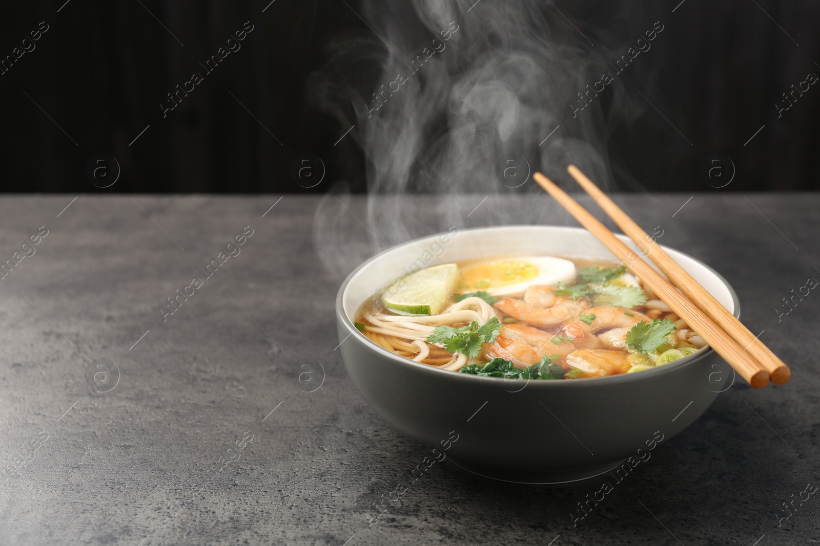 Image of Delicious hot ramen with shrimps and chopsticks on grey table, space for text. Noodle soup