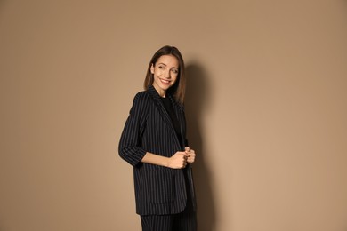 Portrait of beautiful young woman in fashionable suit on beige background. Business attire