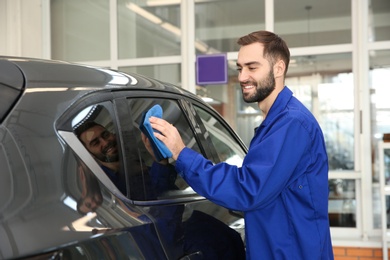 Photo of Worker cleaning automobile window with rag at car wash