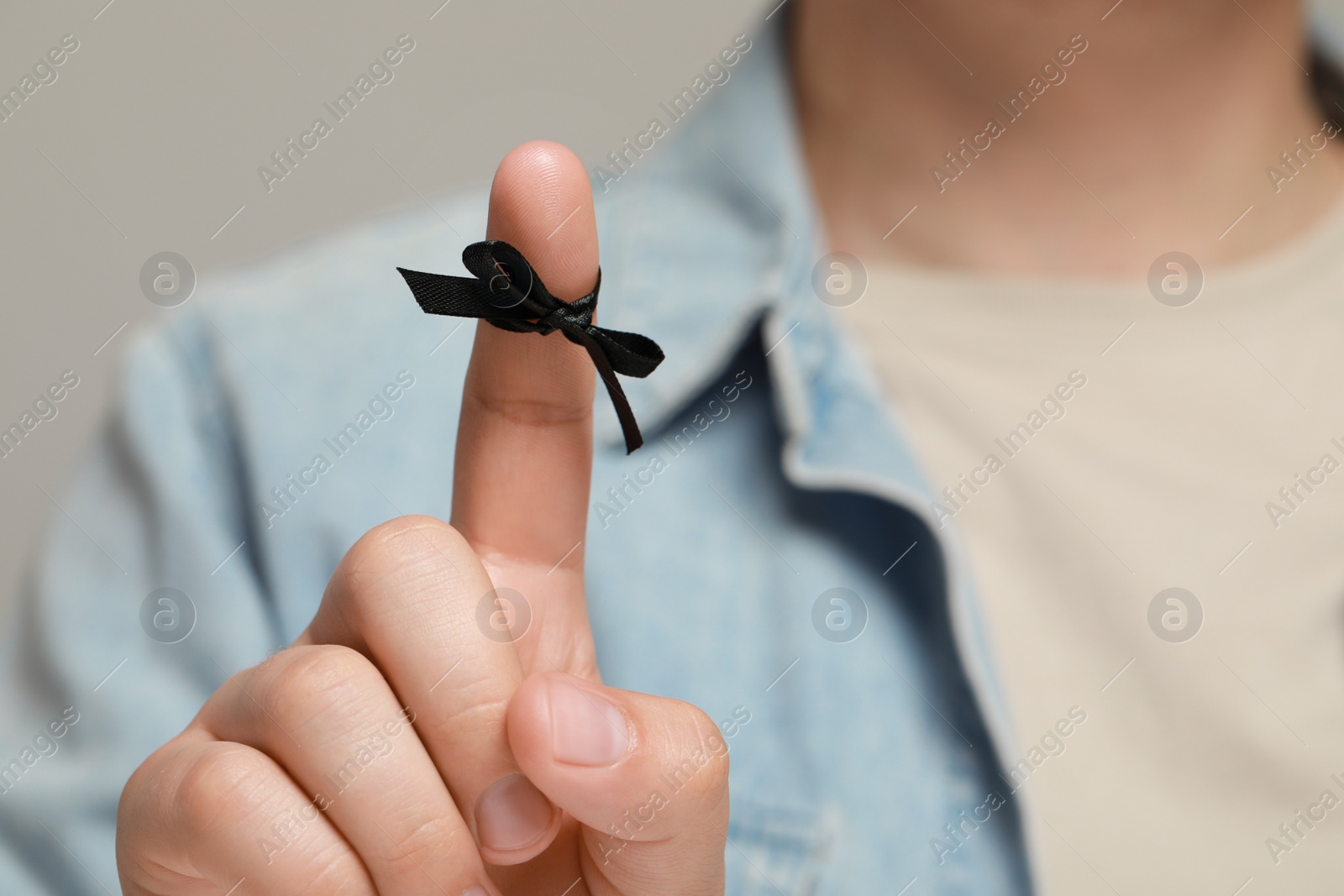 Photo of Man showing index finger with tied bow as reminder against light grey background, focus on hand