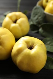 Photo of Fresh ripe organic quinces with leaves on black table, closeup
