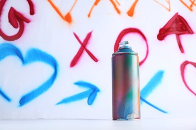 One spray paint can near white wall with different drawn symbols, space for text