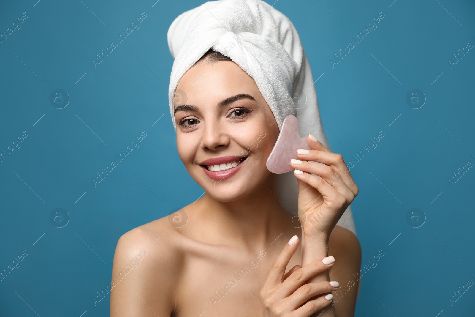 Photo of Beautiful young woman doing facial massage with gua sha tool on blue background