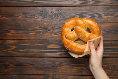 Woman with tasty freshly baked pretzel at wooden table, top view. Space for text