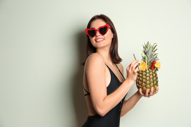Beautiful woman in stylish swimsuit holding tropical cocktail on light grey background