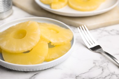 Photo of Tasty canned pineapple slices and fork on white marble table