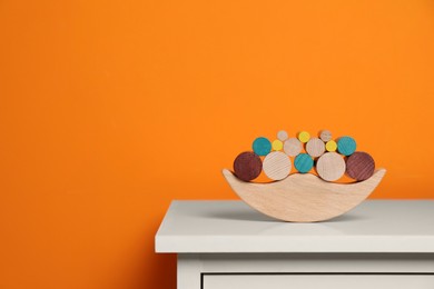 Photo of Wooden balance toy on white chest of drawers near orange wall, space for text. Children's development