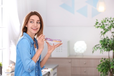 Photo of Beautiful young woman holding plate with donuts in kitchen, space for text. Failed diet