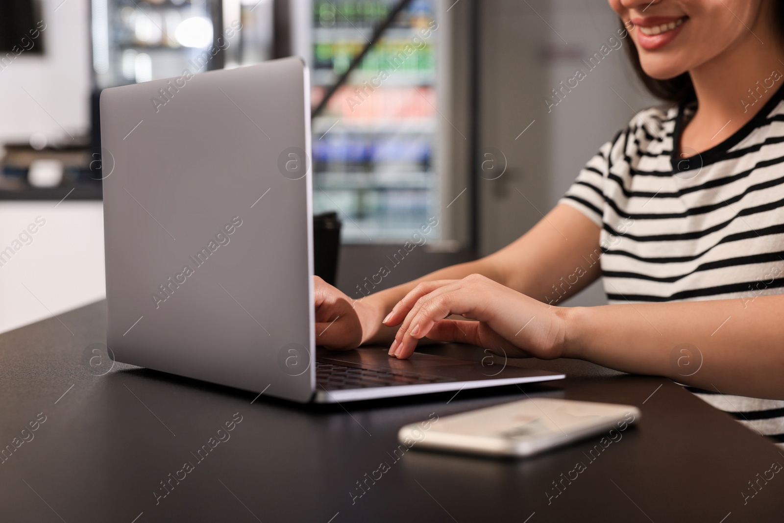 Photo of Happy young woman using laptop at table in hostel dining room, closeup