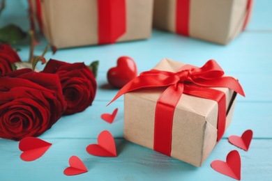 Photo of Beautiful gift box, roses and paper hearts on turquoise wooden table. Valentine's Day celebration