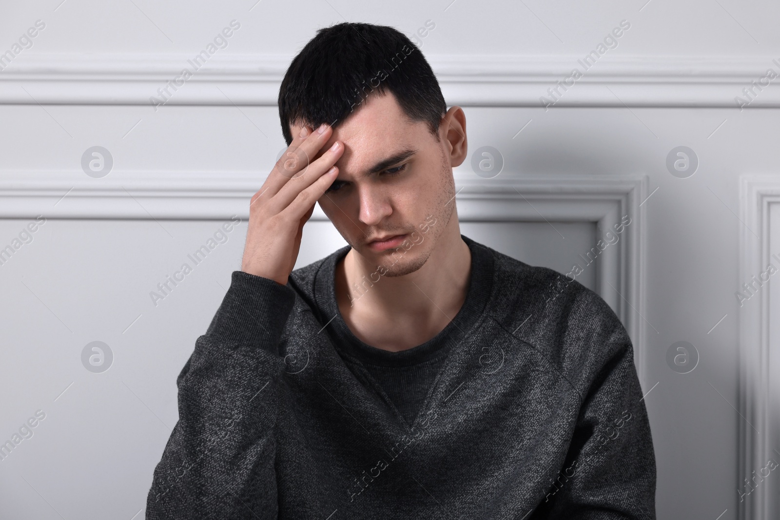 Photo of Sad man sitting near white wall indoors