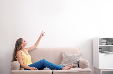 Photo of Young woman with air conditioner remote at home