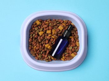Photo of Glass bottle of tincture and dry pet food in bowl on light blue background, top view