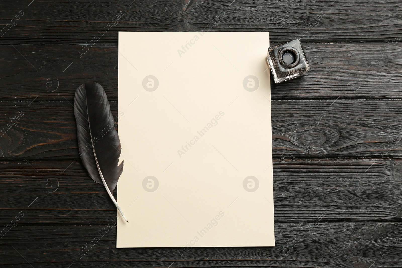 Photo of Feather pen, inkwell and blank parchment on wooden table, top view. Space for text