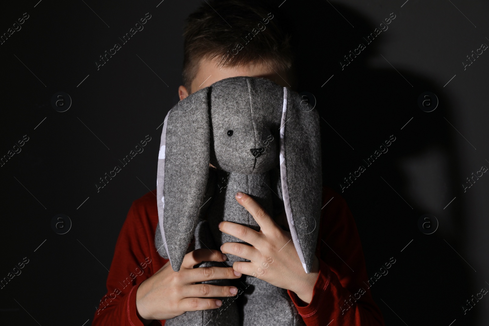 Photo of Little boy with toy near black wall. Domestic violence concept