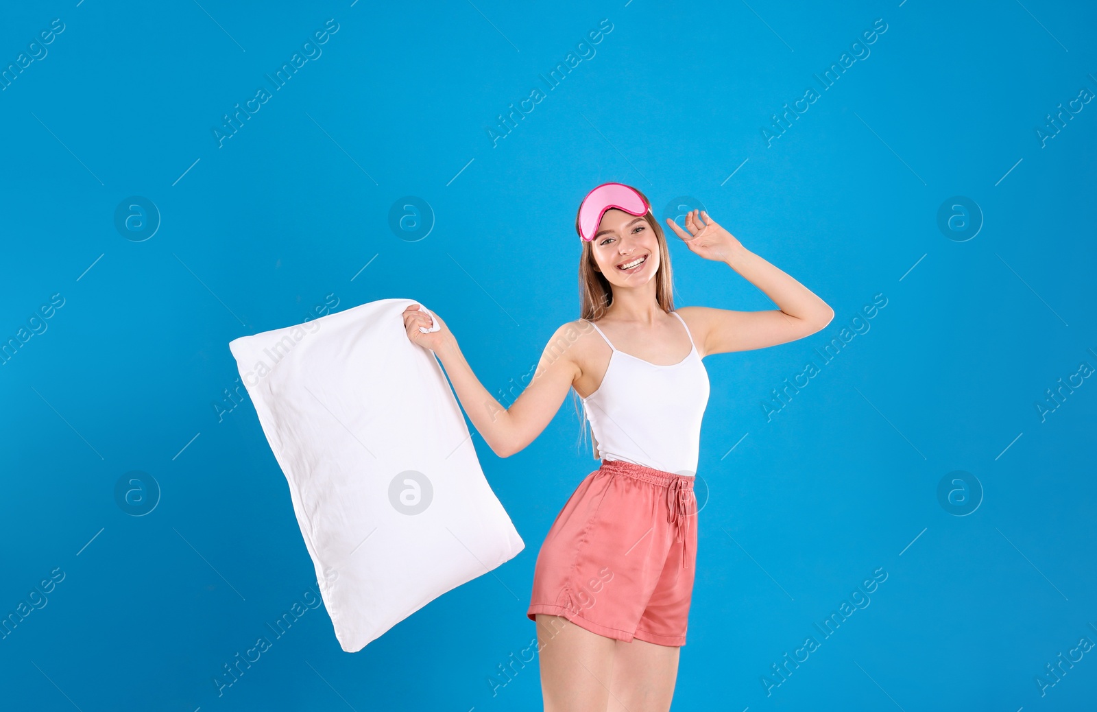 Photo of Young woman with pillow and sleep mask on blue background