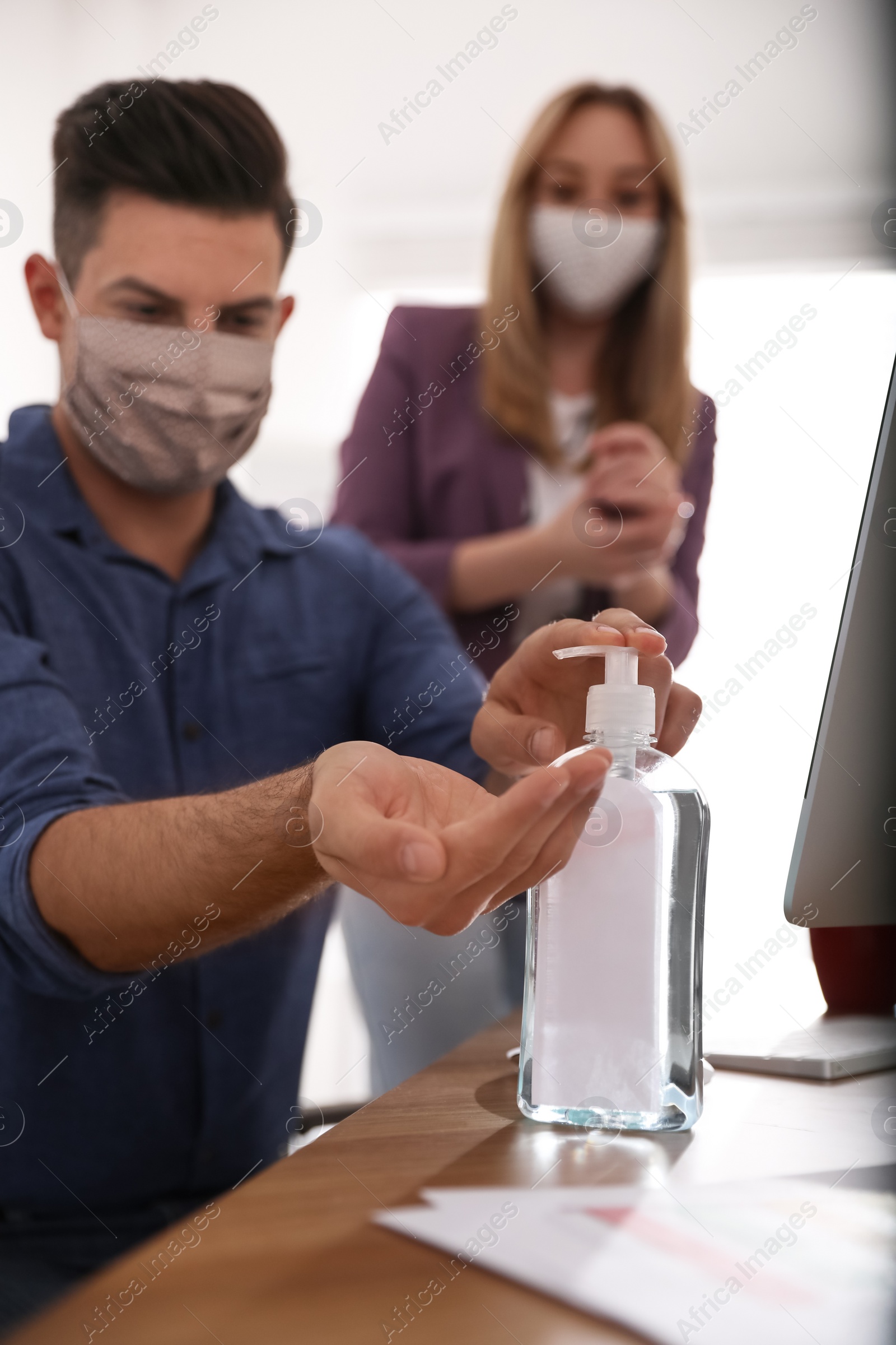 Photo of Office worker using sanitizer at table, focus on hands. Personal hygiene during COVID-19 pandemic