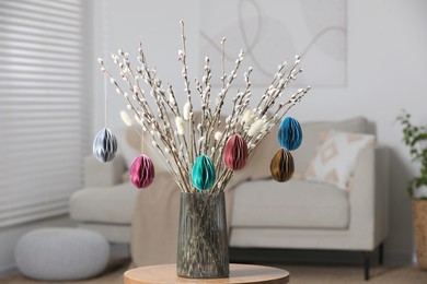 Photo of Beautiful pussy willow branches with paper eggs in vase on wooden table at home. Easter decor