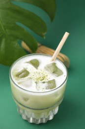 Photo of Glass of tasty iced matcha latte and leaf on green background