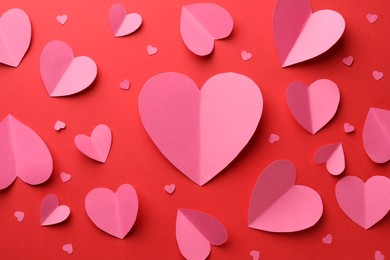 Pink paper hearts on red background, flat lay