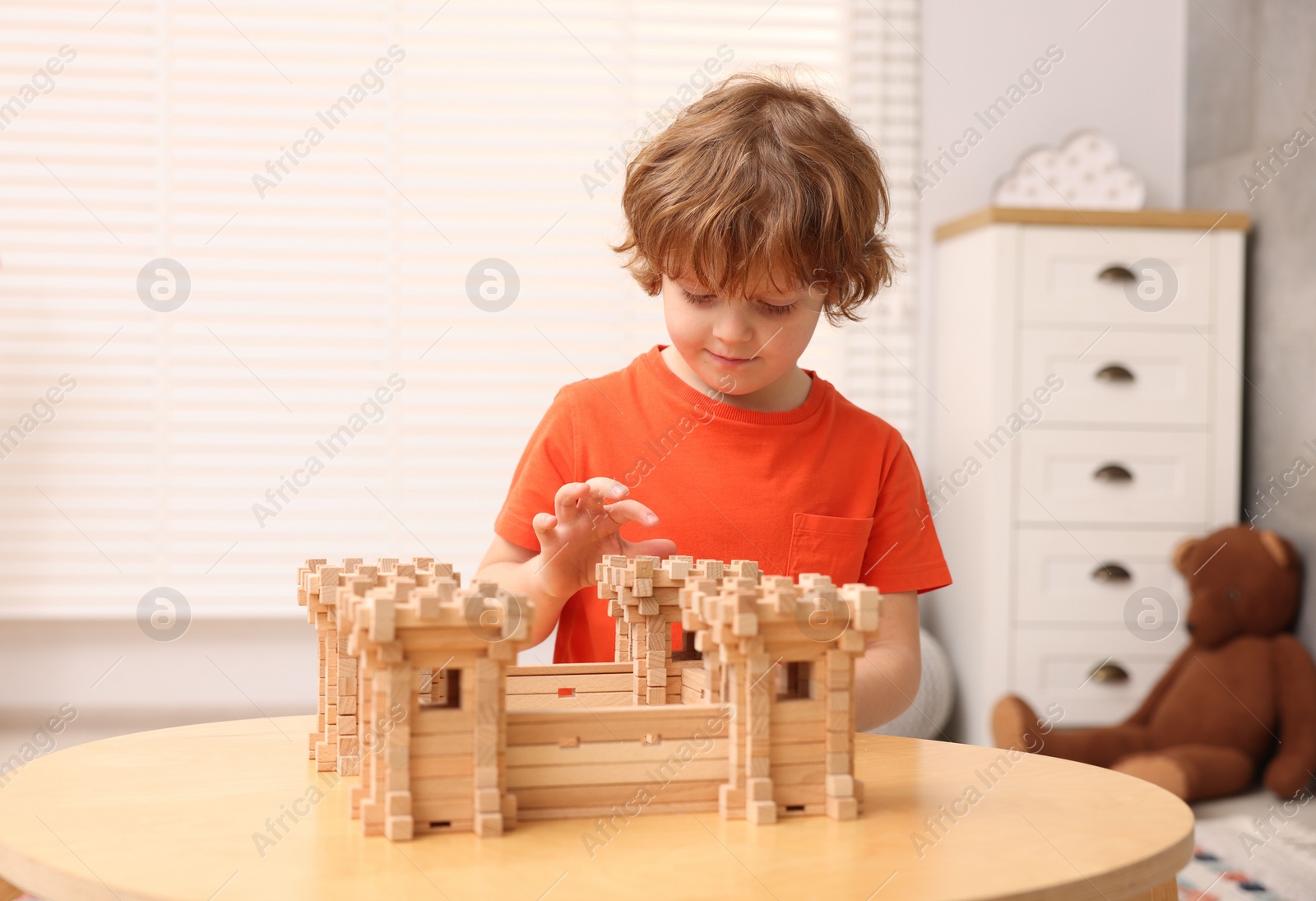 Photo of Cute little boy playing with wooden fortress at table in room. Child's toy