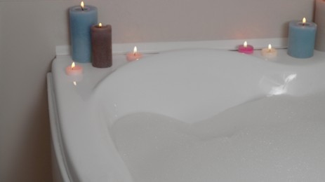 Photo of Hot tub with foam and burning candles in dark bathroom