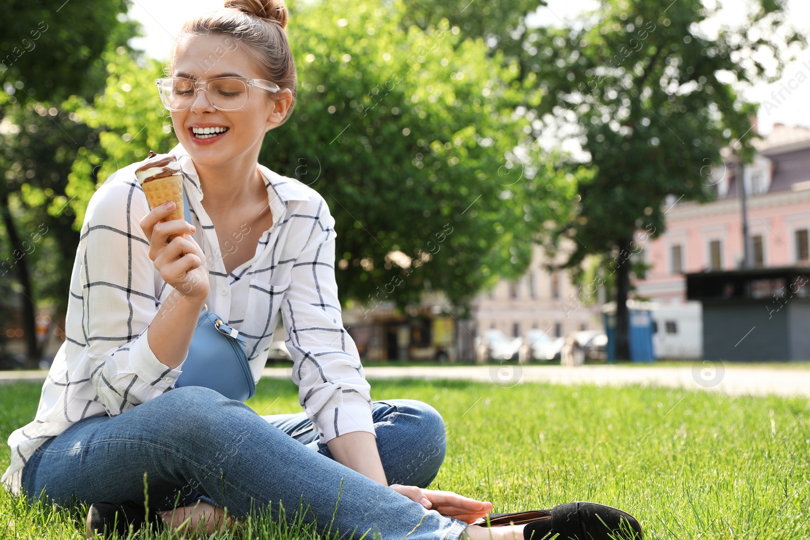 Photo of Young happy woman with ice cream sitting on grass in park. Space for text