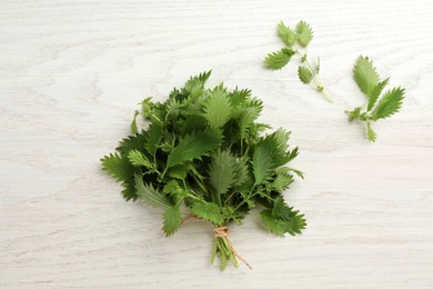 Photo of Bunch of fresh stinging nettles on white wooden table, flat lay