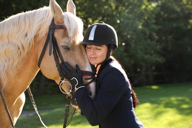 Young woman in horse riding suit and her beautiful pet outdoors on sunny day