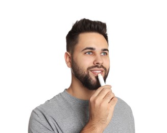 Photo of Young man applying lip balm on white background