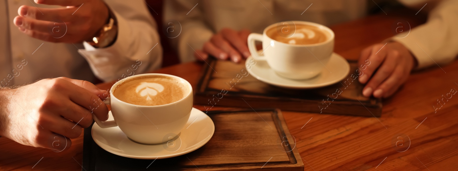 Image of People with cups of aromatic coffee at wooden table, closeup. Banner design