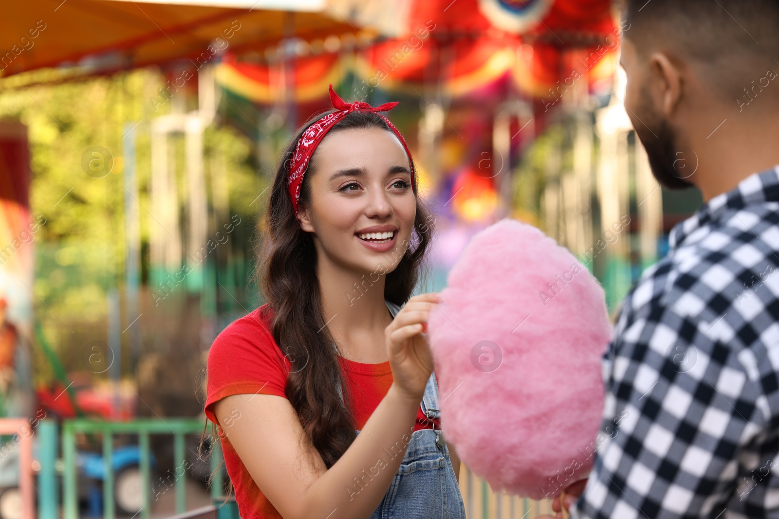 Photo of Happy young woman taking piece of cotton candy from his boyfriend at funfair