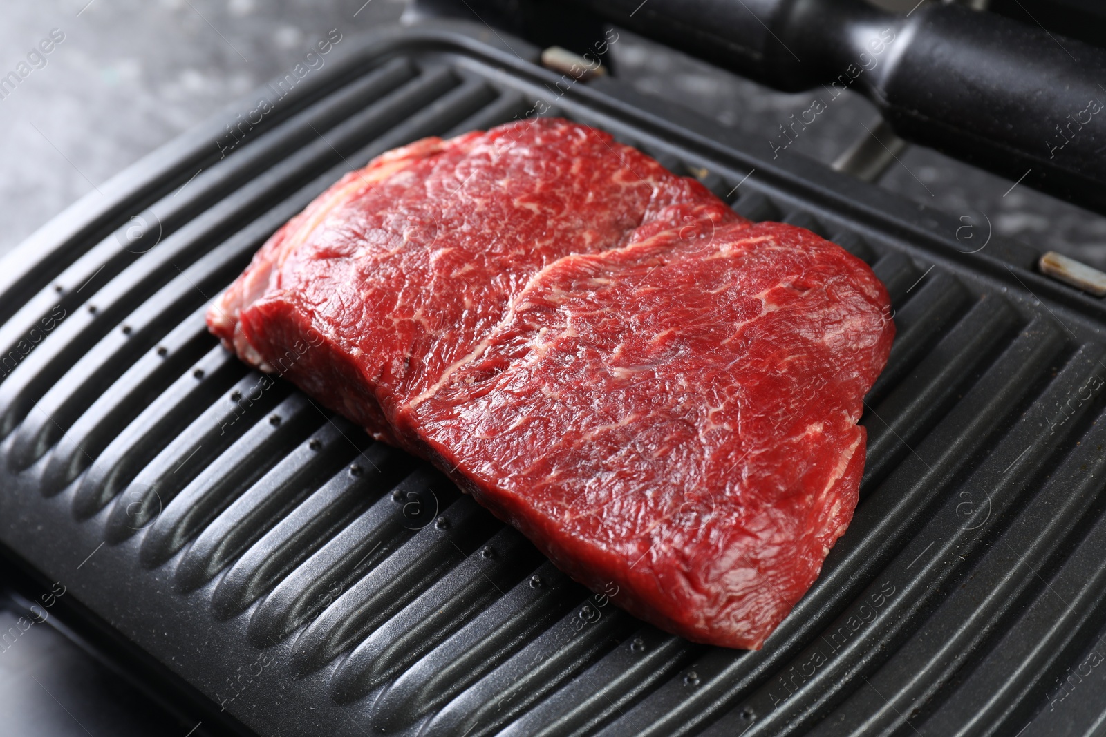 Photo of Cooking fresh beef cut on electric grill, closeup