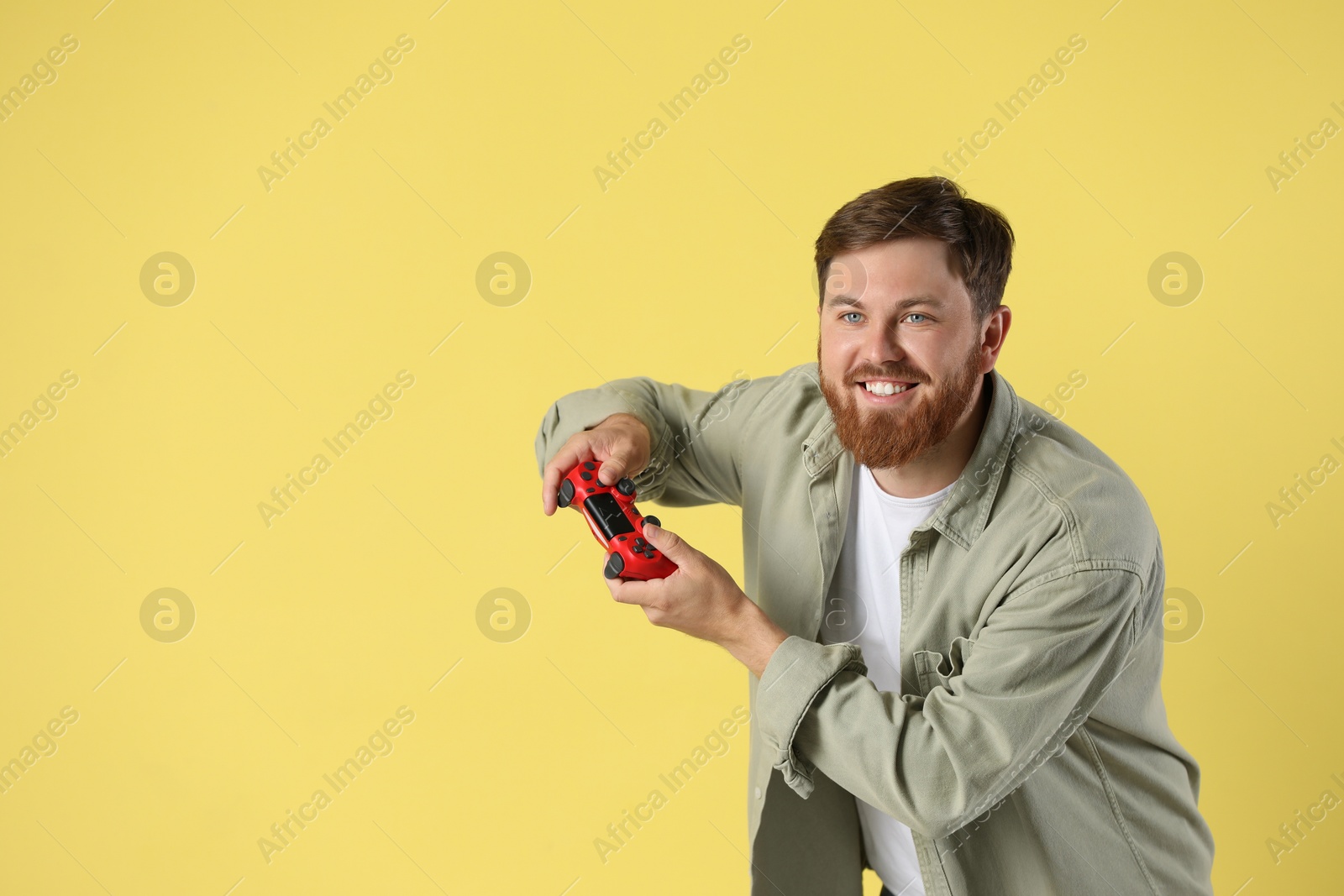 Photo of Happy man playing video game with controller on pale yellow background. Space for text