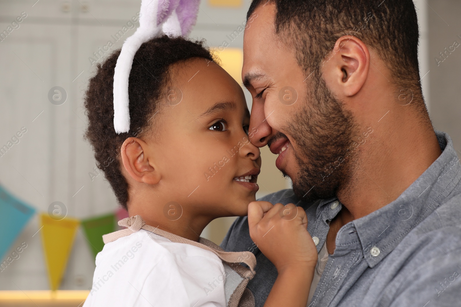 Photo of Happy African American father and his cute son in bunny ears headband indoors. Easter celebration