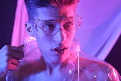 Photo of Stylish young man wearing clear coat and glasses in neon lights