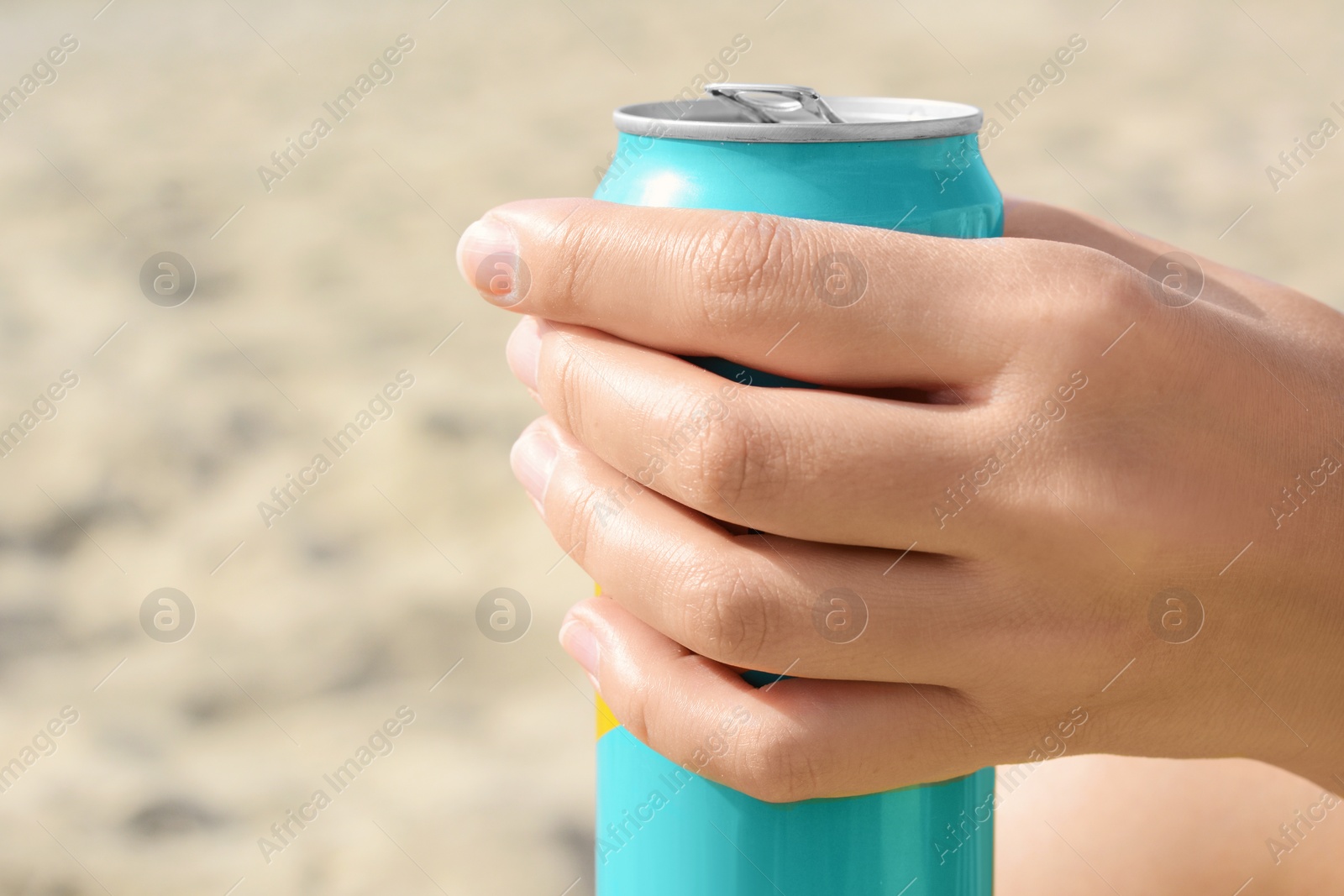 Photo of Woman holding aluminum can with beverage on sand, closeup. Space for text