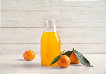 Photo of Fresh tangerines and bottle of juice on white wooden table