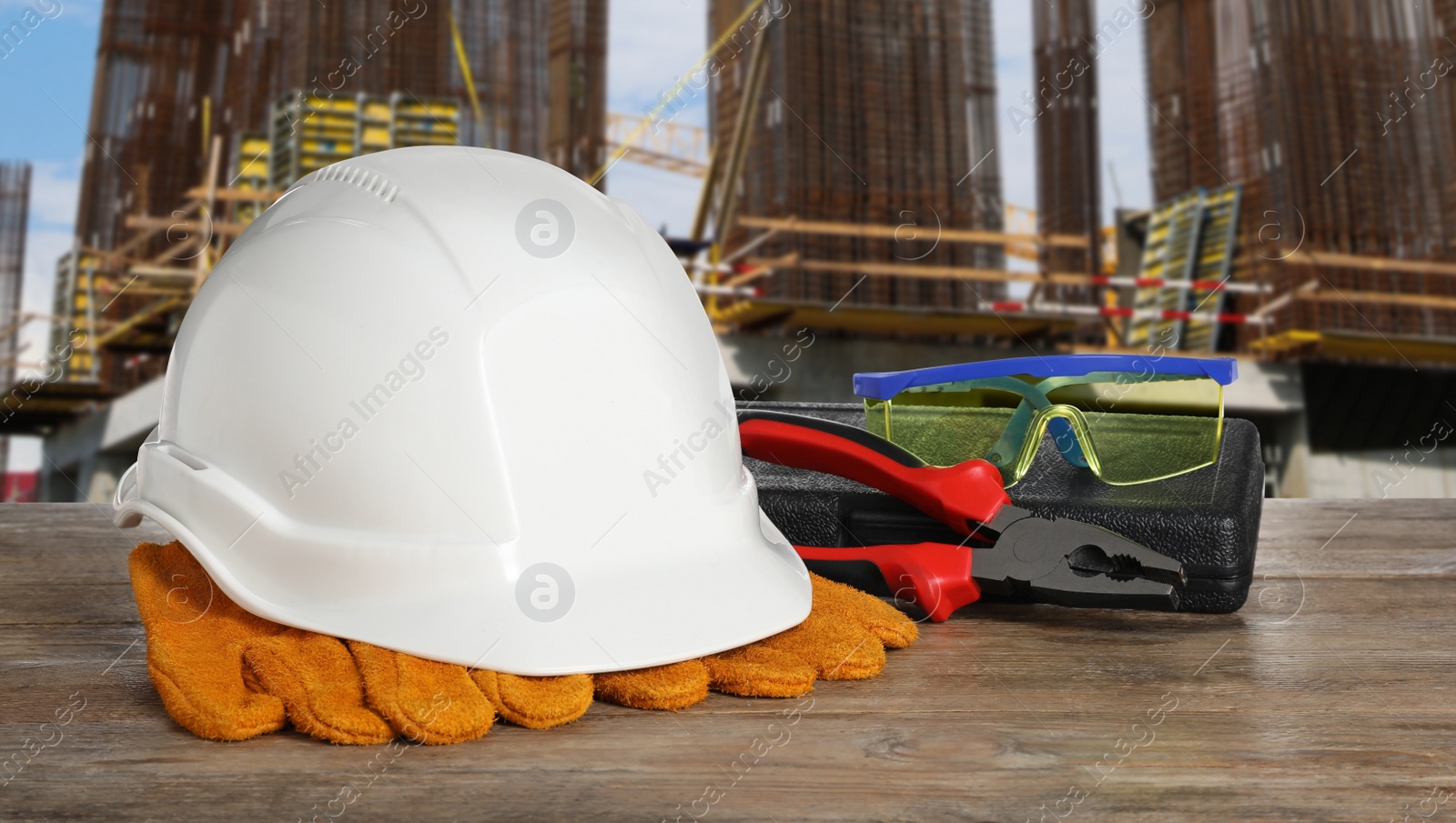 Image of Safety equipment and tools on wooden surface and blurred view of construction site