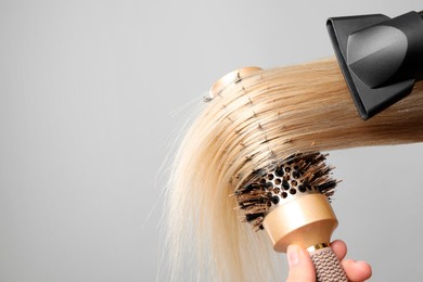 Photo of Hairdresser blow drying client's hair on light grey background, closeup. Space for text