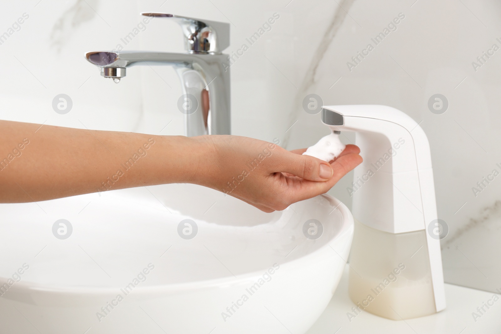 Photo of Woman using automatic soap dispenser in bathroom, closeup