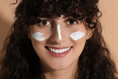 Beautiful young woman with sun protection cream on her face against beige background, closeup