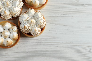 Photo of Many different tartlets with meringue on white wooden table, flat lay and space for text. Tasty dessert