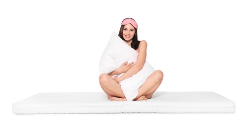 Photo of Young woman in sleeping mask on soft mattress holding pillow against white background