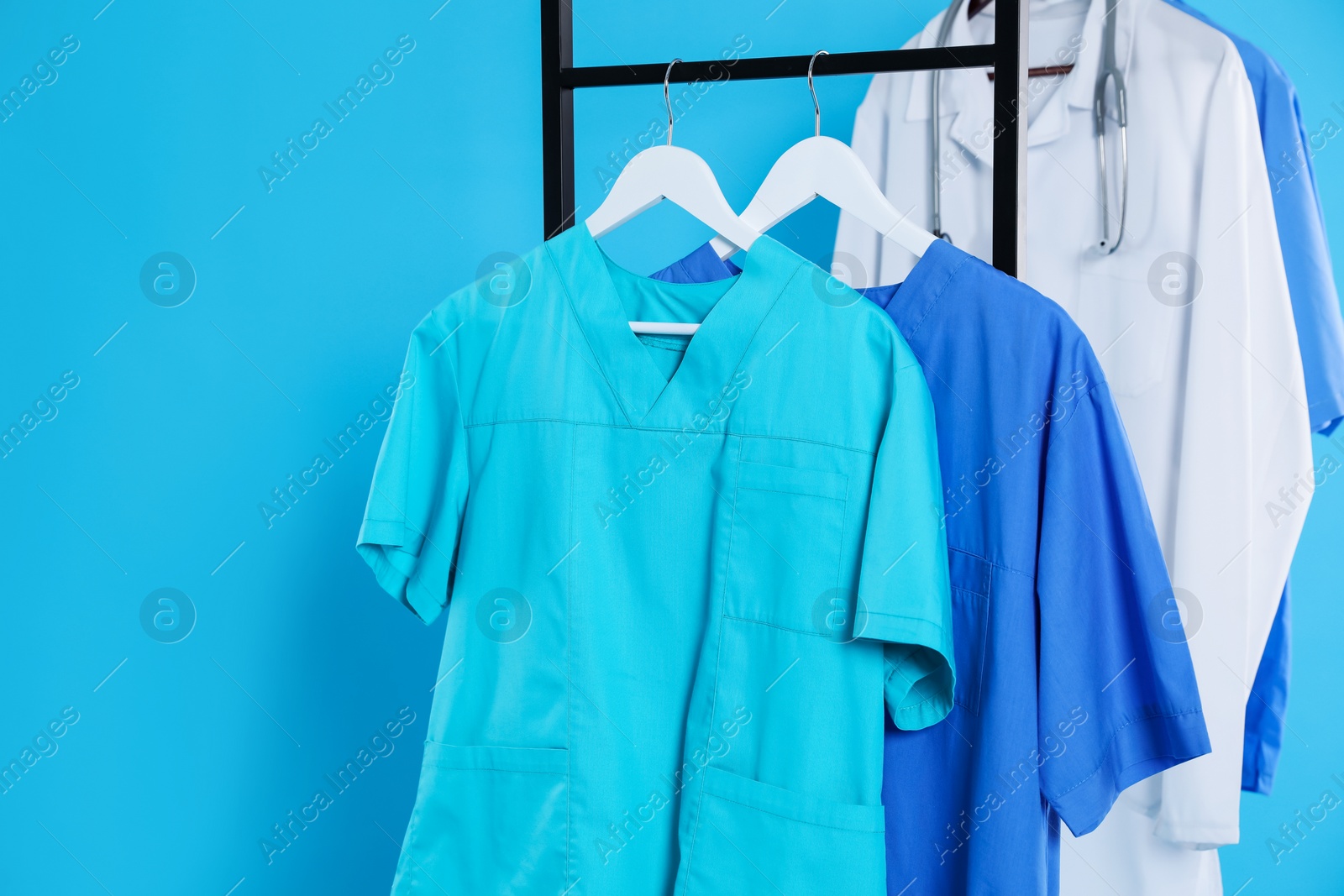 Photo of Medical uniforms on metal rack against light blue background